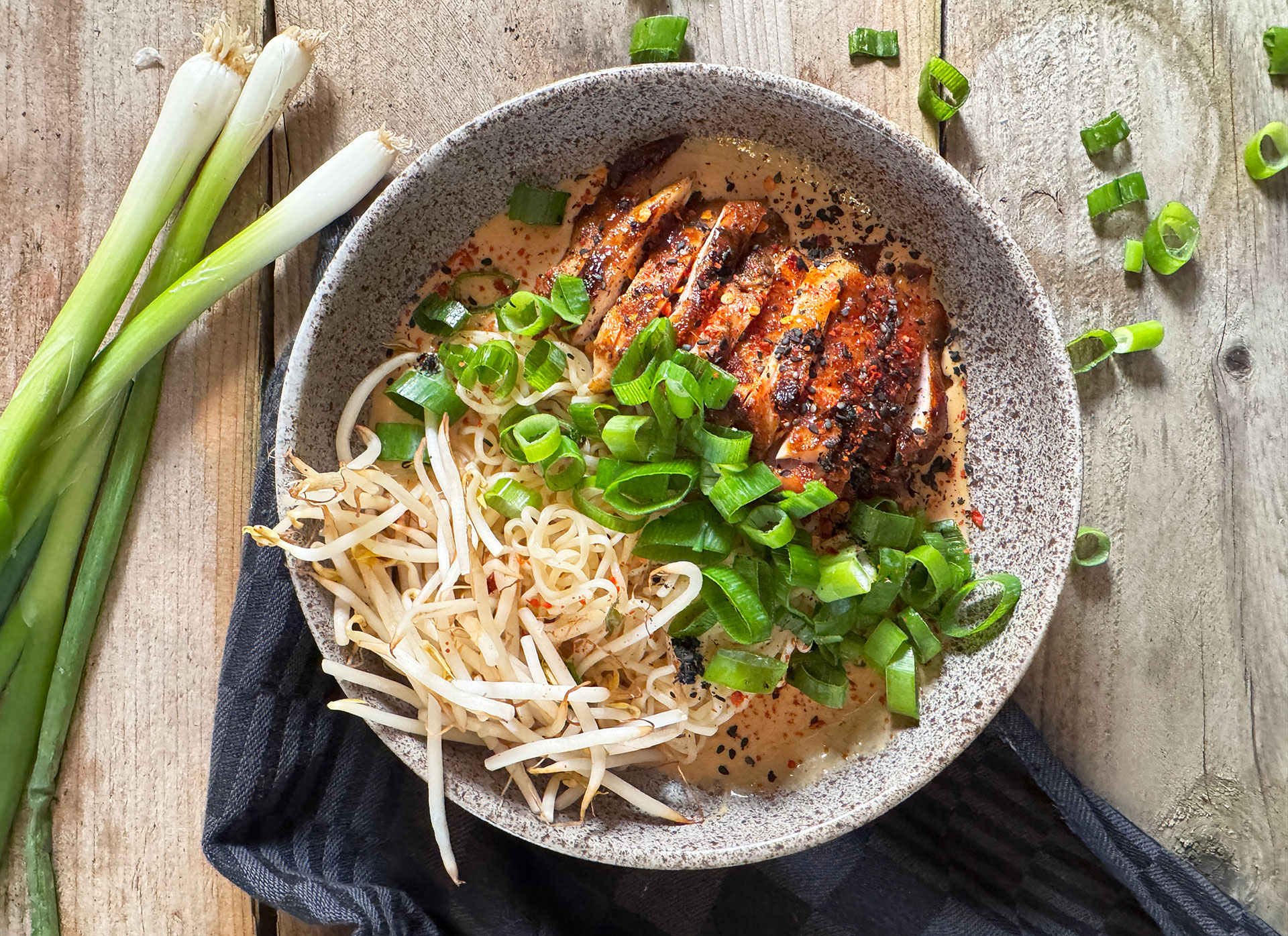 Een kom met Japanse ramen noodles, spicy kip en romige knoflooksaus, gegarneerd met bosui en taugé